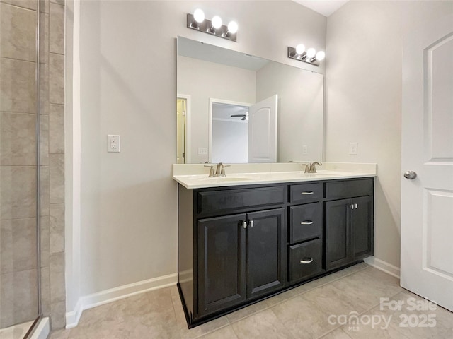 bathroom featuring double vanity, tiled shower, a sink, and baseboards