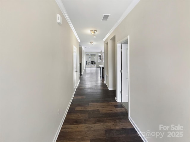 hall featuring dark wood-style floors, baseboards, visible vents, and ornamental molding