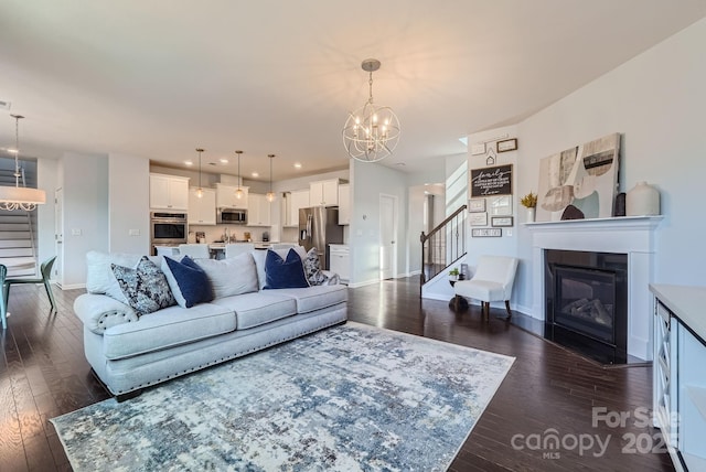 living room with a notable chandelier, dark wood finished floors, baseboards, stairway, and a glass covered fireplace