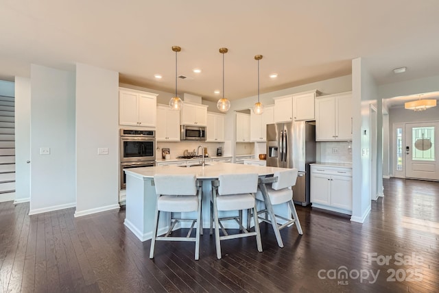 kitchen featuring dark wood-style floors, a center island with sink, stainless steel appliances, light countertops, and a kitchen breakfast bar