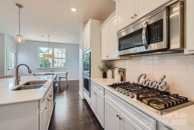 kitchen featuring stainless steel appliances, a sink, white cabinetry, backsplash, and dark wood finished floors