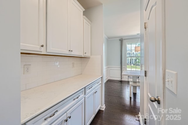 kitchen with light stone counters, a wainscoted wall, white cabinetry, decorative backsplash, and dark wood-style floors