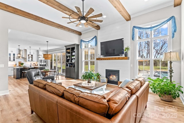 living room featuring a large fireplace, baseboards, ceiling fan, beamed ceiling, and light wood-type flooring