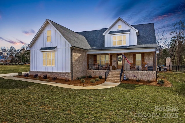 modern inspired farmhouse featuring board and batten siding, covered porch, a lawn, and brick siding