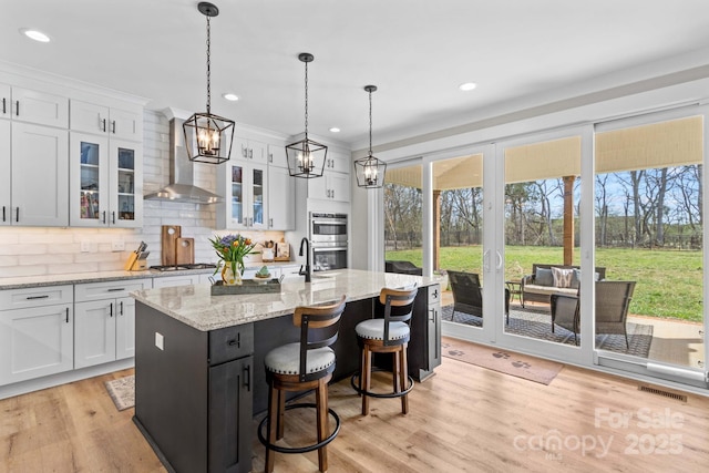 kitchen featuring tasteful backsplash, visible vents, white cabinets, light wood-style flooring, and wall chimney range hood