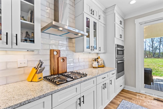 kitchen featuring stainless steel appliances, wall chimney range hood, light stone counters, and white cabinetry