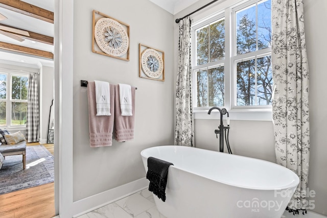 full bathroom with marble finish floor, a freestanding bath, beamed ceiling, and baseboards