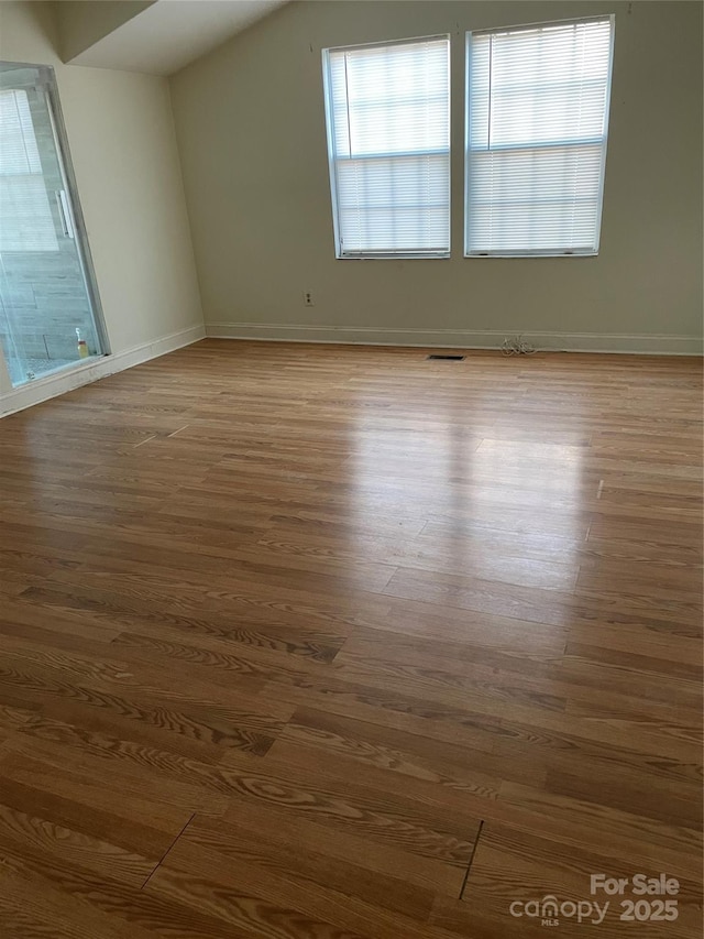 unfurnished room featuring vaulted ceiling, wood finished floors, and visible vents