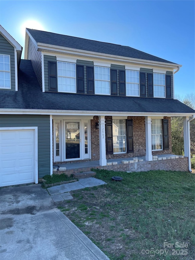 view of front of home featuring concrete driveway, roof with shingles, a front yard, a porch, and brick siding