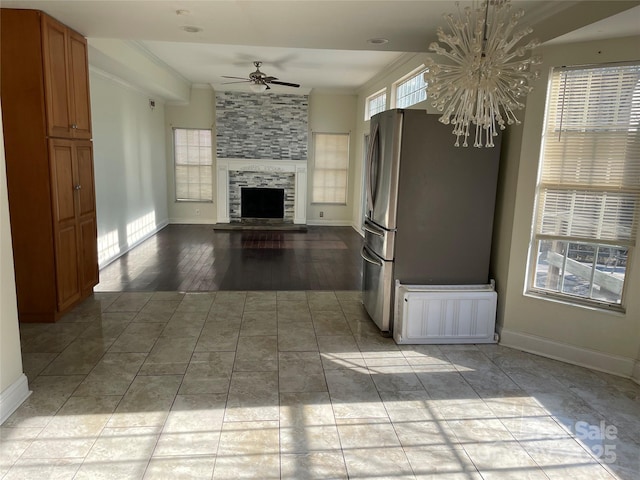 unfurnished living room featuring a large fireplace, baseboards, crown molding, and ceiling fan with notable chandelier