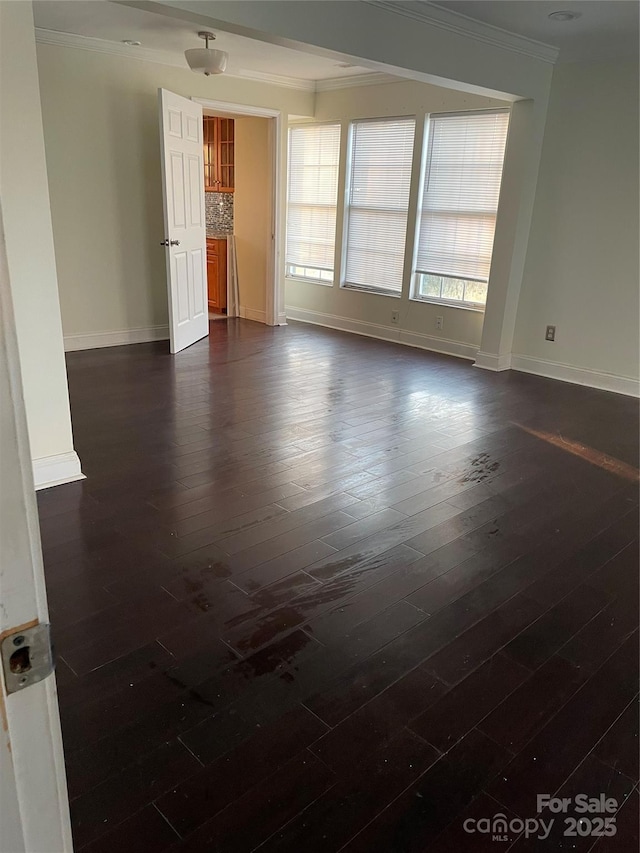 spare room with ornamental molding, dark wood-style flooring, and baseboards