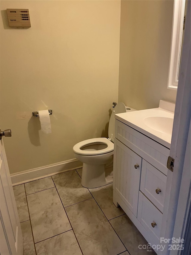 half bathroom featuring vanity, toilet, and baseboards