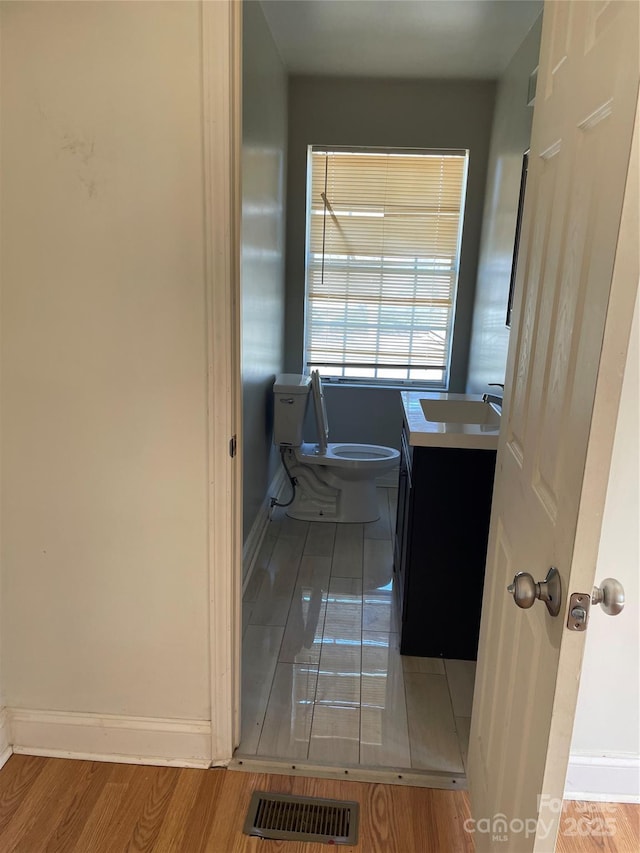 half bath featuring visible vents, toilet, vanity, wood finished floors, and baseboards