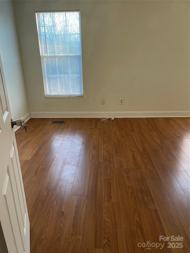 unfurnished room with baseboards, visible vents, and wood finished floors