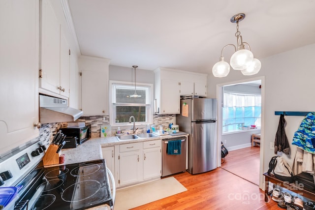 kitchen with a sink, light countertops, under cabinet range hood, appliances with stainless steel finishes, and white cabinetry