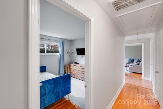 hallway featuring attic access, wood finished floors, visible vents, and baseboards