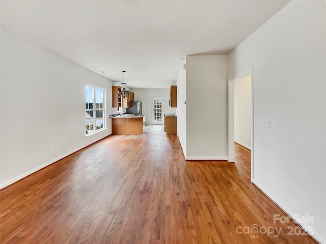 unfurnished living room with a notable chandelier, light wood-style flooring, and baseboards