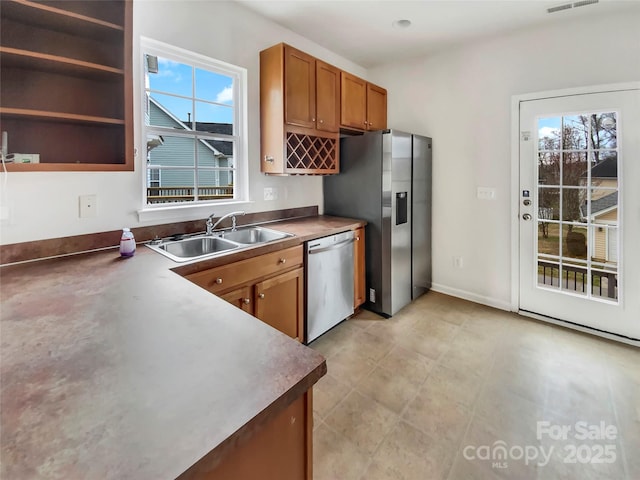 kitchen featuring stainless steel appliances, brown cabinets, a sink, and baseboards