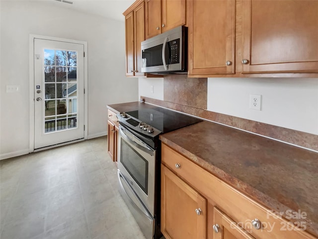 kitchen featuring visible vents, brown cabinetry, baseboards, dark countertops, and stainless steel appliances