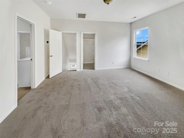 unfurnished bedroom featuring carpet floors, baseboards, visible vents, and a walk in closet