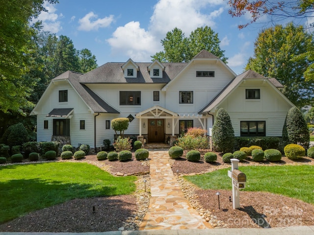 view of front facade with stone siding, roof with shingles, and a front yard