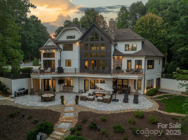 back of house with a shingled roof, a fire pit, fence, a chimney, and a patio