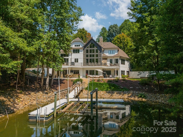 rear view of house featuring a water view, a balcony, a chimney, and fence