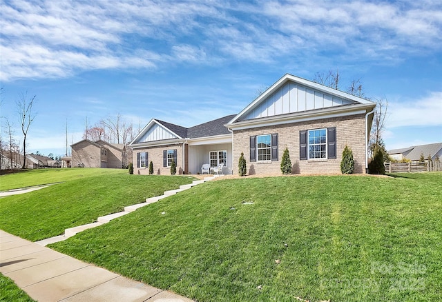 view of front of house featuring board and batten siding, a front yard, and brick siding