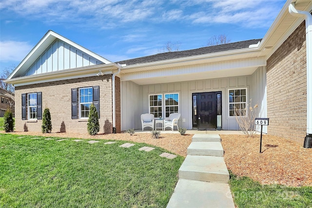 view of exterior entry featuring board and batten siding, brick siding, and a yard