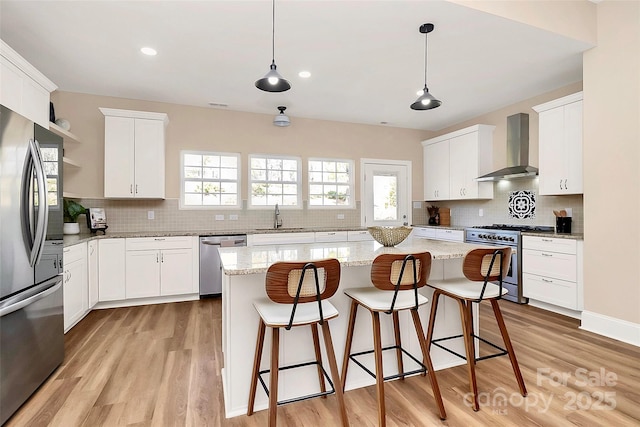 kitchen featuring stainless steel appliances, a breakfast bar, a sink, light wood-style floors, and wall chimney range hood