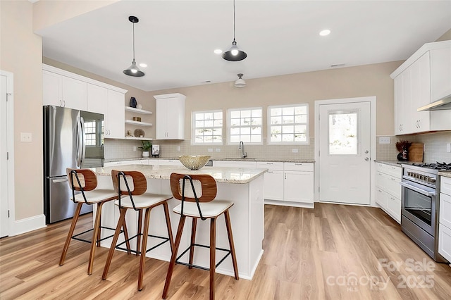 kitchen with a breakfast bar, a kitchen island, appliances with stainless steel finishes, light wood-type flooring, and open shelves