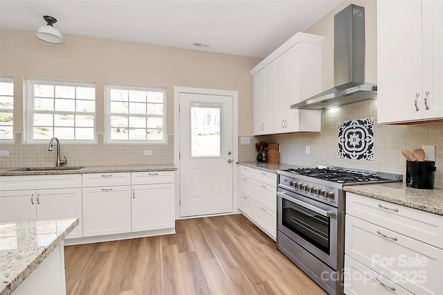 kitchen with visible vents, stainless steel range, light wood-style flooring, wall chimney range hood, and a sink