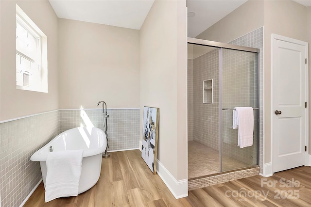 bathroom with a stall shower, a freestanding tub, tile walls, and wood finished floors