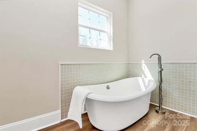 full bath with a soaking tub, wainscoting, tile walls, and wood finished floors