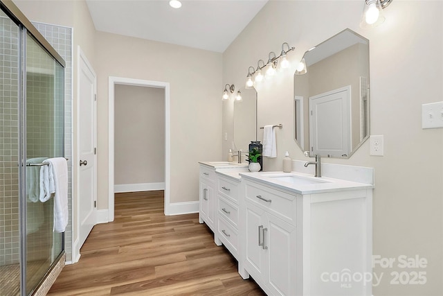 full bathroom featuring double vanity, wood finished floors, a sink, and a shower stall