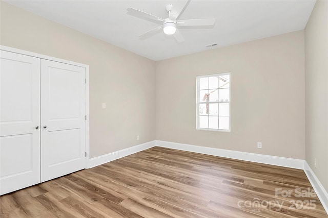 empty room featuring a ceiling fan, wood finished floors, visible vents, and baseboards