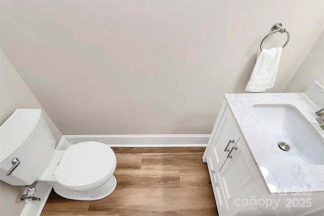 half bathroom featuring toilet, wood finished floors, vanity, and baseboards