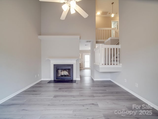 unfurnished living room featuring visible vents, baseboards, a fireplace with flush hearth, wood finished floors, and stairs