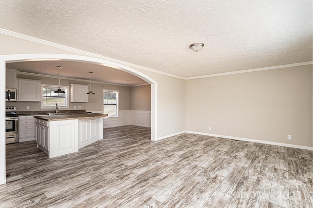 kitchen featuring arched walkways, stainless steel appliances, wood finished floors, open floor plan, and ornamental molding