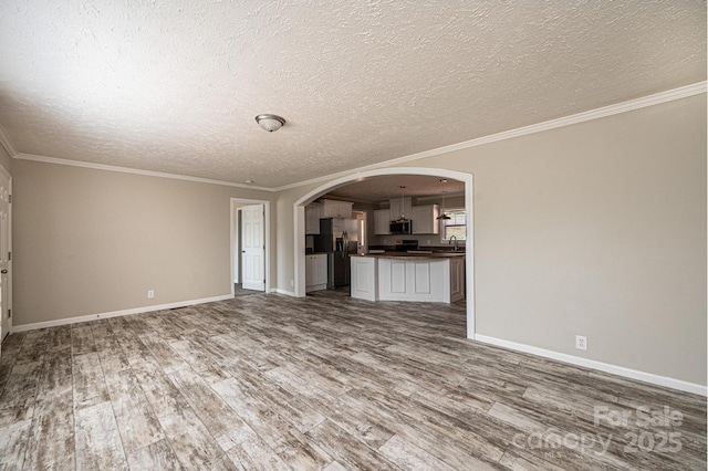 unfurnished living room featuring arched walkways, ornamental molding, wood finished floors, and baseboards