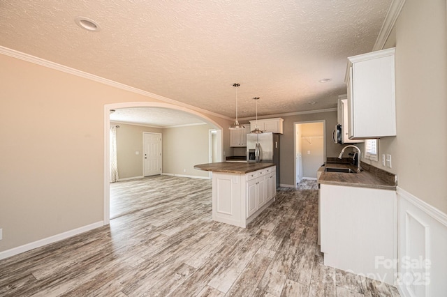 kitchen featuring arched walkways, stainless steel refrigerator with ice dispenser, dark countertops, a kitchen island, and a sink