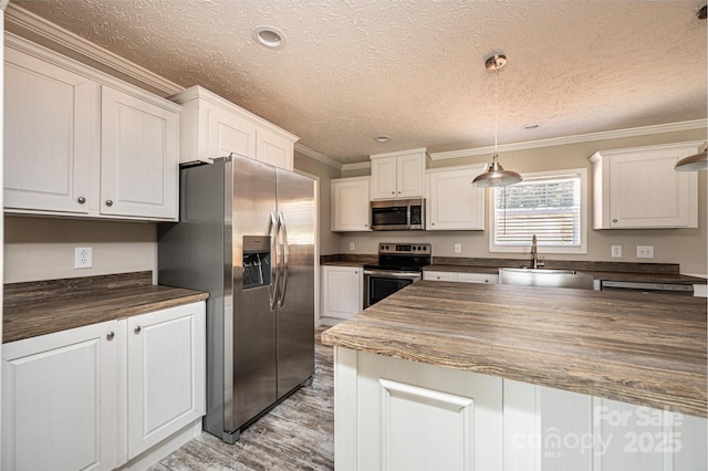 kitchen with wooden counters, appliances with stainless steel finishes, ornamental molding, white cabinets, and a sink