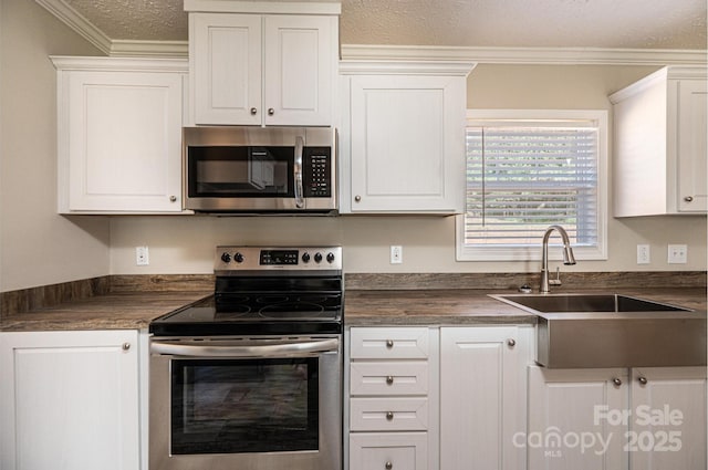 kitchen featuring appliances with stainless steel finishes, dark countertops, a sink, and white cabinetry