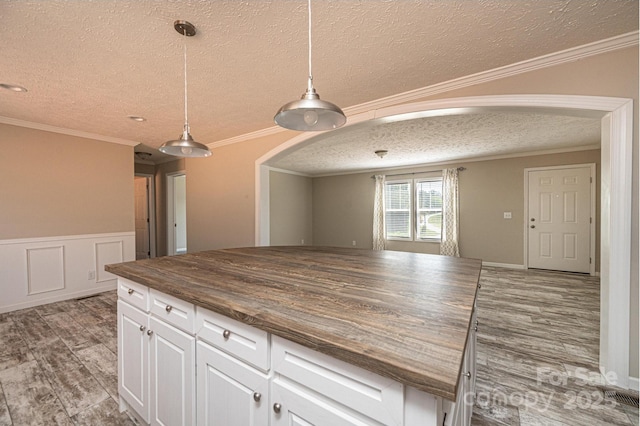 kitchen featuring arched walkways, a wainscoted wall, crown molding, white cabinets, and wood finished floors