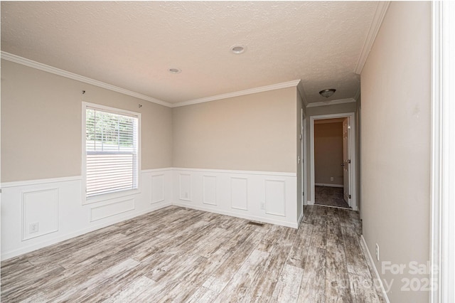 spare room with a textured ceiling, a wainscoted wall, wood finished floors, and crown molding