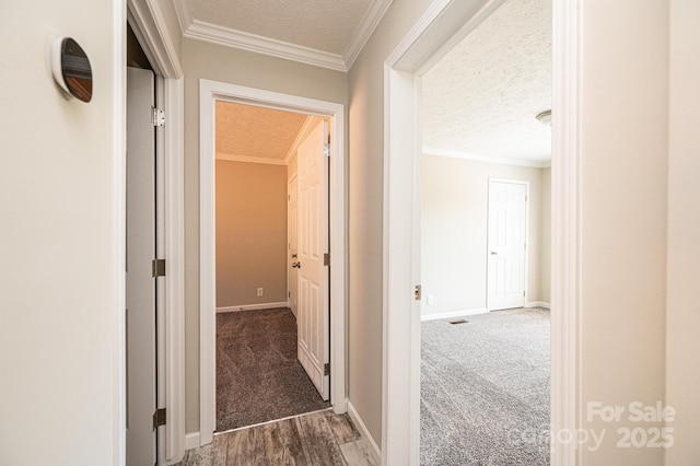 corridor featuring carpet floors, ornamental molding, a textured ceiling, and baseboards