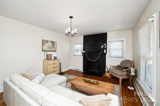 living room featuring baseboards, a fireplace with flush hearth, dark wood-style flooring, an inviting chandelier, and a baseboard heating unit