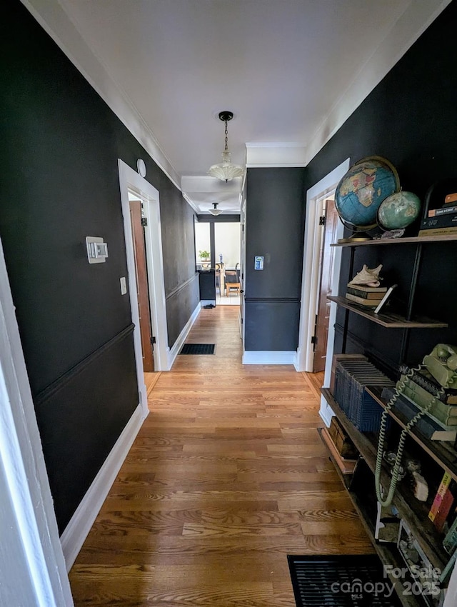 corridor featuring light wood-type flooring, visible vents, crown molding, and baseboards