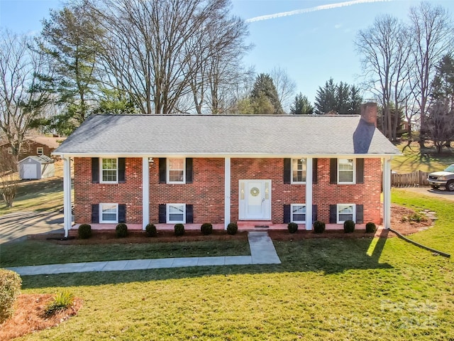 raised ranch featuring roof with shingles, a front lawn, a chimney, and brick siding