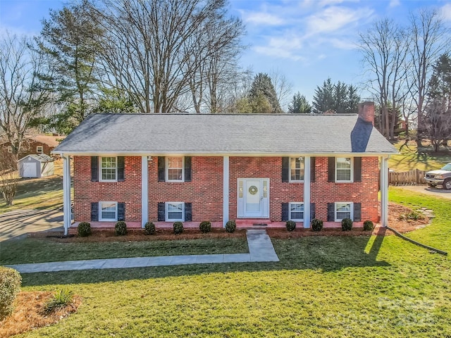 bi-level home featuring roof with shingles, a front lawn, a chimney, and brick siding